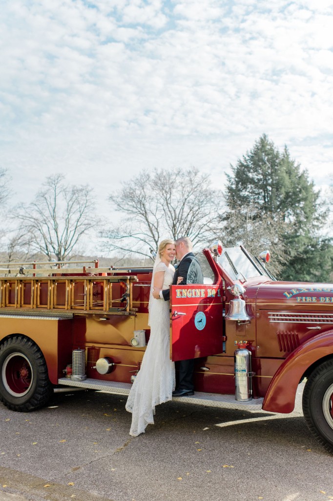 A bride and groom kissing beside the open door of a vintage red fire engine