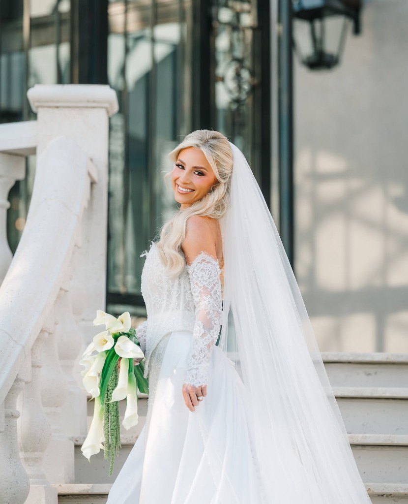 A bride in an ivory lace gown and veil, looking back on stone steps with a bouquet of calla lilies