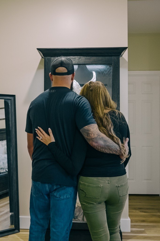 A couple standing together in front of a Mrs. Case, looking at the gown inside