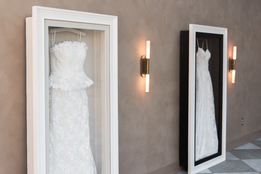 Two wall-mounted Mrs. Case Gallery frames displaying lace gowns on a plaster wall