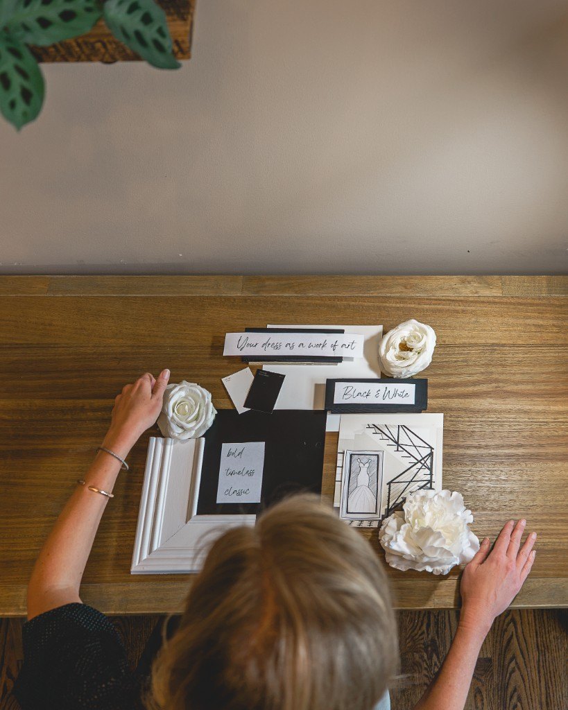 Hands arranging a white frame, roses, and Black and White samples on a wood table