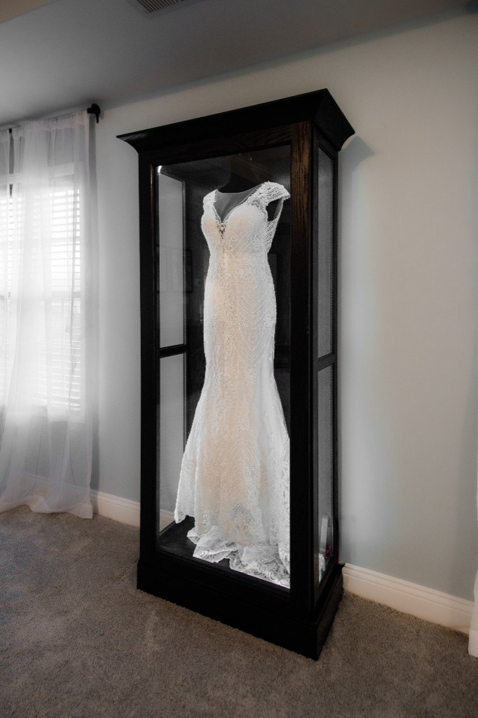 A freestanding Mrs. Case Signature displaying a lace gown in a bedroom beside sheer curtains