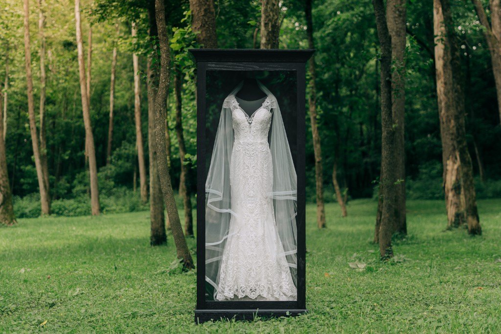 A freestanding Mrs. Case Signature displaying a gown on a green lawn among trees