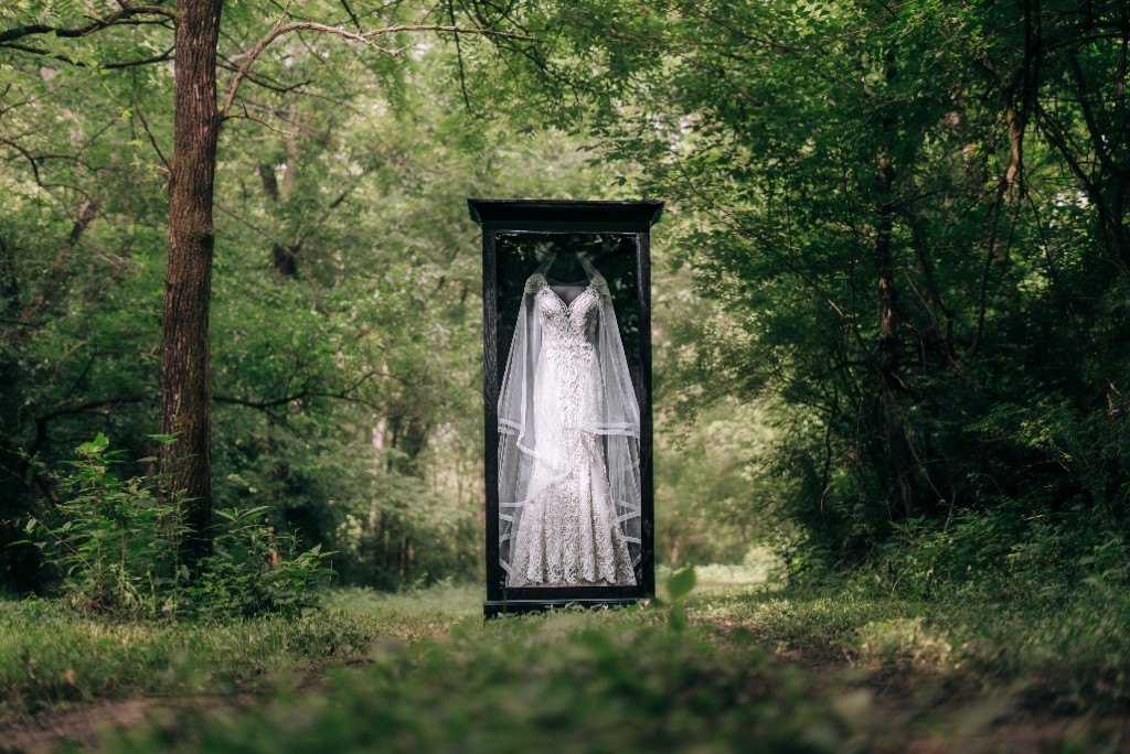 A freestanding Mrs. Case Signature displaying a lace gown and veil in a green wood