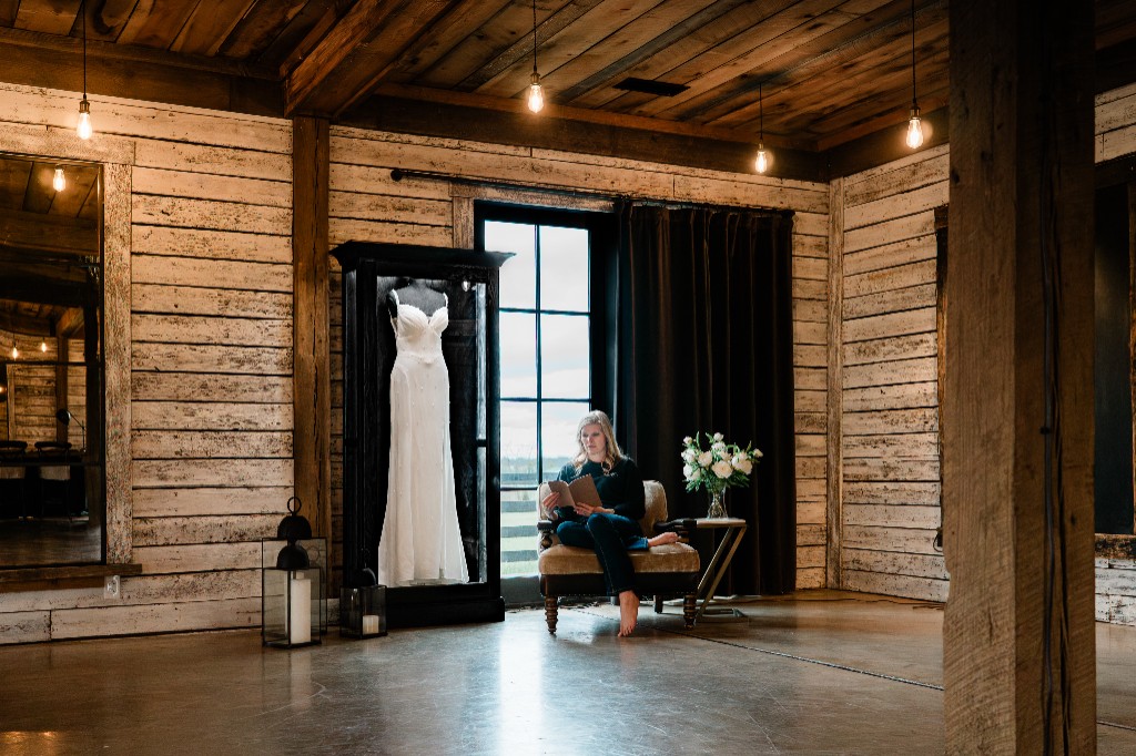 A woman reading beside a freestanding Mrs. Case displaying a gown in a timber room